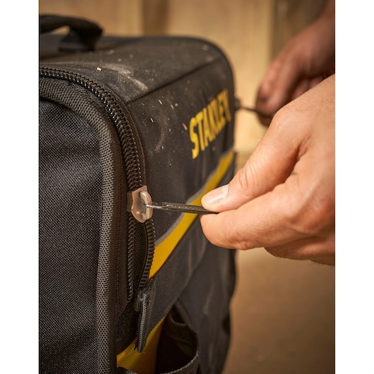 STANLEY 1-97-515 tool bag photography, close-up of hand using zipper on black and yellow fabric bag.