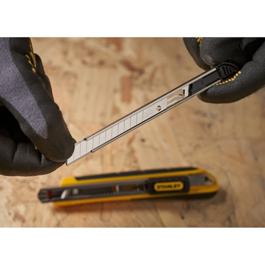 Photo of STANLEY 2-11-300 snap-off utility knife blade being inserted, with gloved hands, on a wood surface.