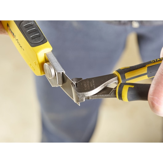 STANLEY 2-11-725 utility knife and side cutter pliers cutting metal piece, close-up view.