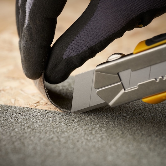 STANLEY 2-11-725 utility knife cutting roofing material, close-up view, gloved hand holding material.
