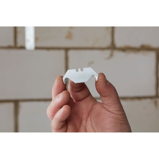 Photo of STANLEY 2-11-983 hook blade held in hand, used for cutting, shown against tiled background.