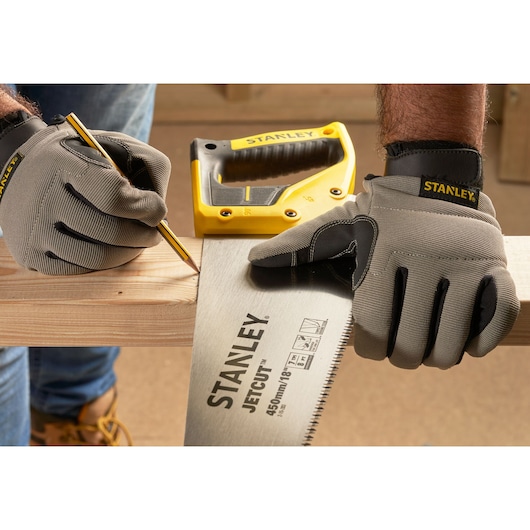 STANLEY 2-15-283 hand saw with yellow handle held by gloved hands, marking wood plank. Photography front angle.