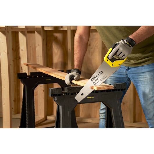 Stanley 2-15-594 hand saw used to cut wood on black Stanley sawhorses in workshop photography.