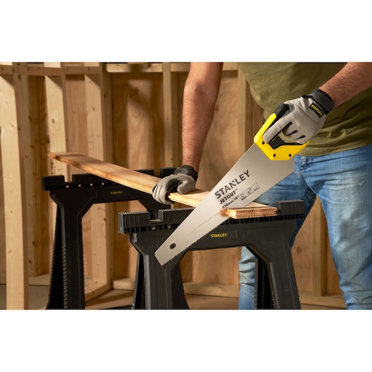 Photo of STANLEY 2-15-595 hand saw cutting wood, person wearing gloves in a workshop setting.