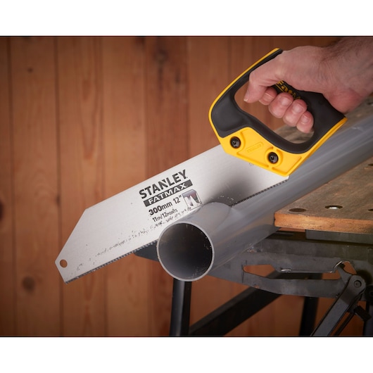STANLEY 2-17-206 hand saw cutting plastic pipe on workbench, close-up view showing handle and blade.