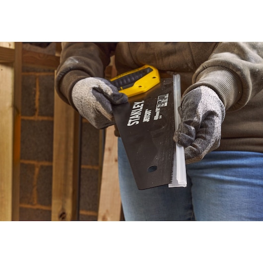 STANLEY 2-20-180 hand saw with yellow and black handle held by gloved hands in workshop setting.