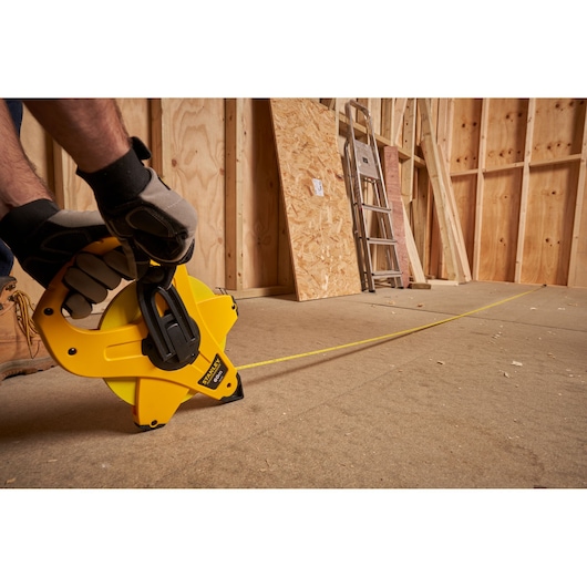 STANLEY 2-34-775 tape measure reel used on construction site, yellow casing, side angle view.