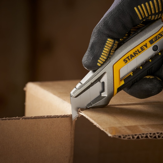 STANLEY 3-11-301 utility knife cutting cardboard, close-up, hand with glove holding the tool.
