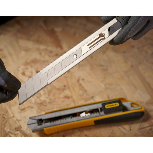 STANLEY 3-11-725 snap-off utility knife blade held above yellow and black utility knife on wood surface.