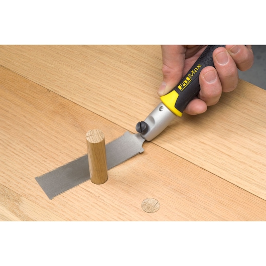 STANLEY 3-20-331 flush cut saw with yellow-black handle cutting wooden dowel on wooden surface.