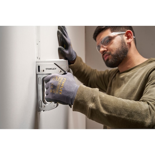 Photo of STANLEY 6-TR110 stapler used on wall by person wearing STANLEY gloves.