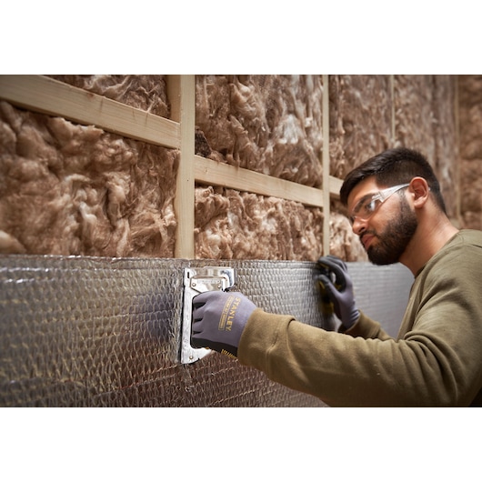 Photo of STANLEY 6-TR45 staple gun being used to attach insulation to a wall, close-up of hand and tool.
