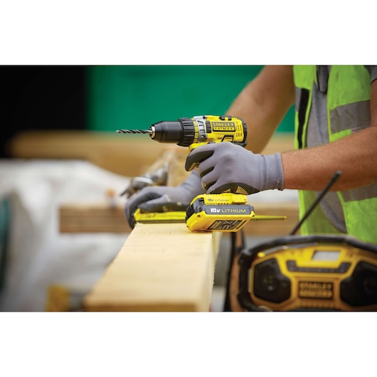 STANLEY FMC600D2 cordless drill being used on wood, close-up view with battery visible, at a construction site.