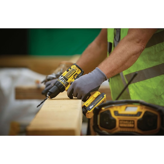 Photo of STANLEY FMC600D2 cordless drill in use on wood at a construction site, worker wearing gloves and safety vest.