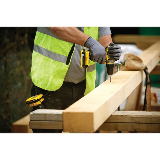 STANLEY FMC600D2 cordless drill used by worker in safety vest, drilling into large wooden beam.