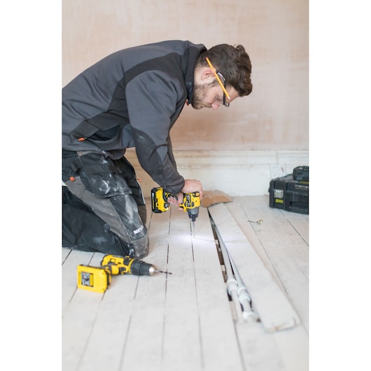 STANLEY FMC647D2T cordless drill in use on wooden floor, worker kneeling with tool box and pipes visible.