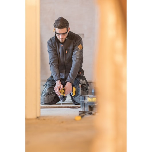 Photo of worker using STANLEY FMC647D2T power tool, kneeling indoors on construction site.