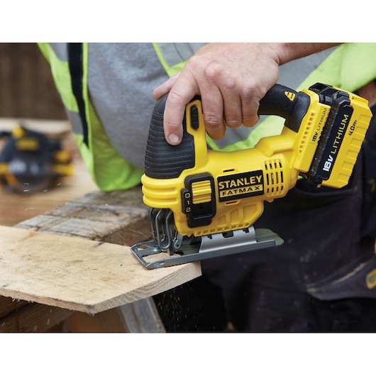 Photo of STANLEY FMC650B yellow cordless jigsaw, cutting wood, showing ergonomic handle and 18V lithium battery.