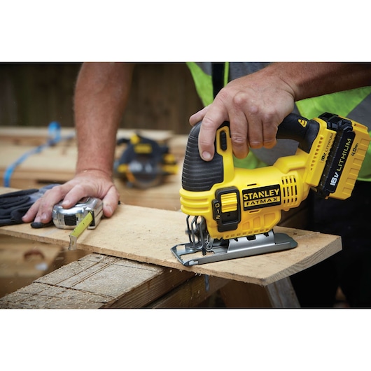STANLEY FMC650M2 cordless jigsaw with 18V lithium battery cutting wood, close-up in workshop setting.
