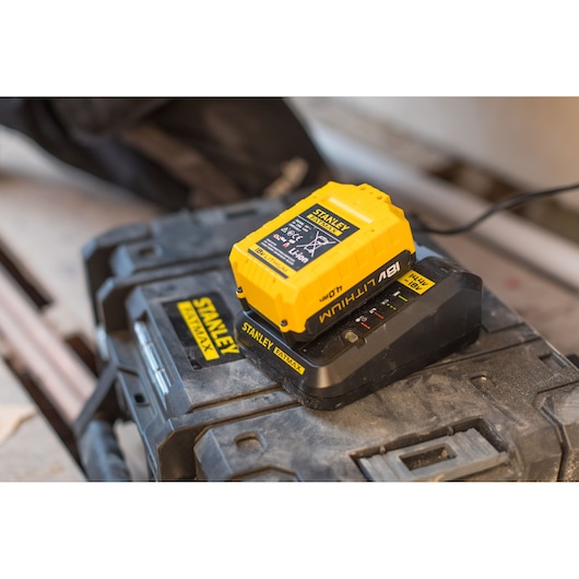 STANLEY FMC688L battery charger with yellow 18V lithium battery on black toolbox, angled view.