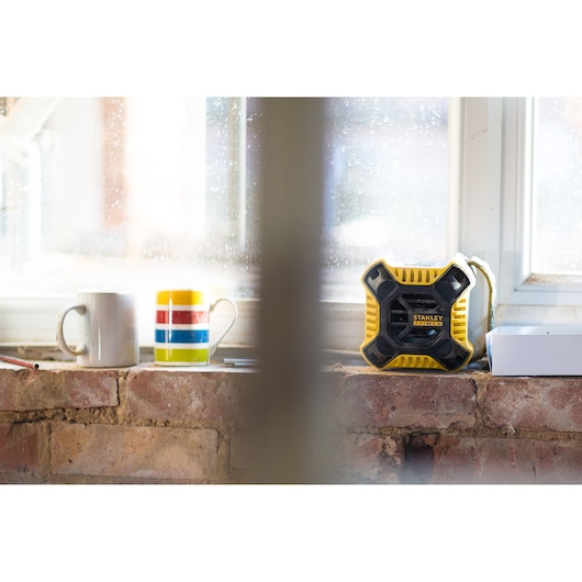 STANLEY FMC772B yellow and black portable speaker on a windowsill next to mugs, side angle.