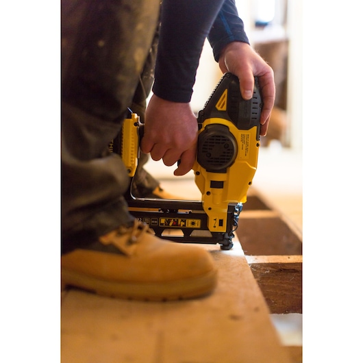 STANLEY FMC792B nailer in use, close-up side view, worker's hands and boot visible on wood surface.