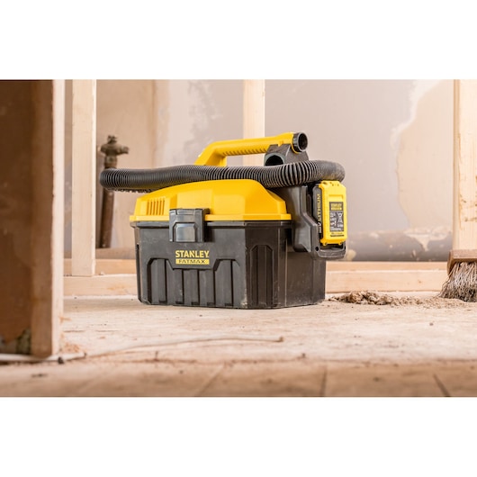 Photo of STANLEY FMC795B wet/dry vacuum showing yellow and black design with hose, used at a construction site.