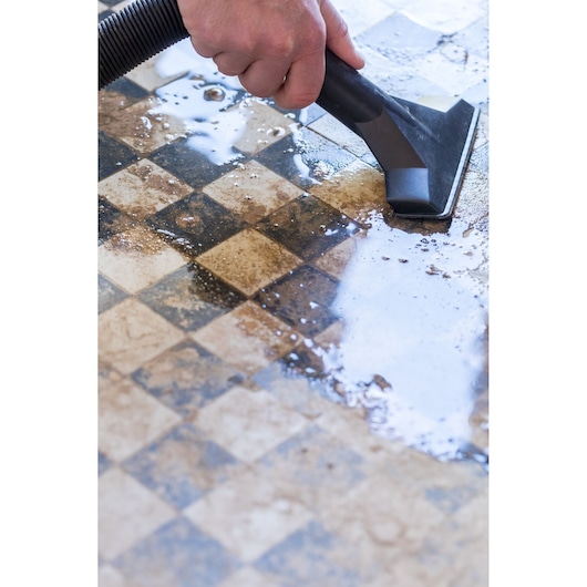 STANLEY FMC795B wet vacuum cleaner nozzle removing water from checkered tile floor, close-up.