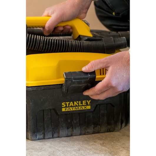 Photo of STANLEY FATMAX FMC795B portable wet dry vacuum with yellow handle and hose, close-up of hands using latch.