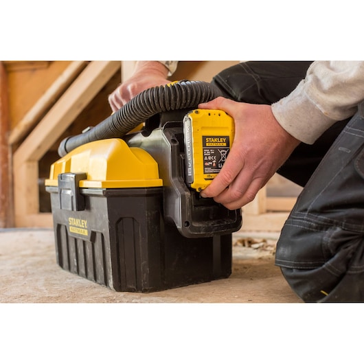 Photo of STANLEY FMC795B portable vacuum with yellow battery pack being installed, used on a jobsite floor.
