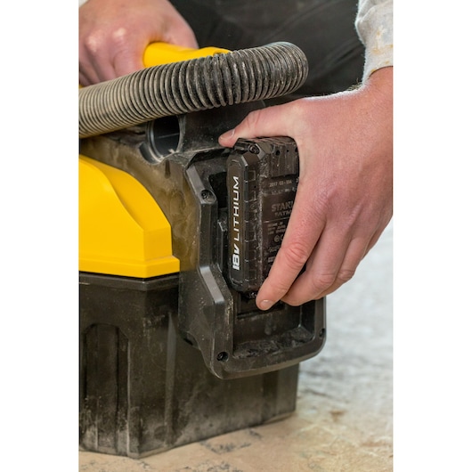 Photo of STANLEY FMC795B vacuum with hand inserting 18V lithium battery, close-up view of battery compartment.