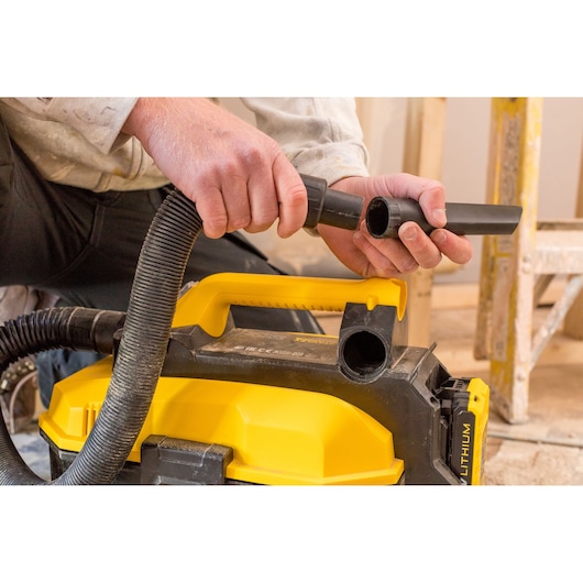 STANLEY FMC795B portable vacuum cleaner, close-up of hose attachment, yellow and black, photo of product in use.