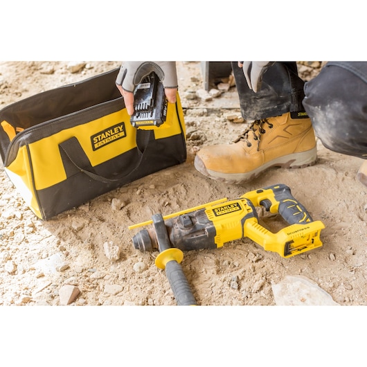 Stanley FMCD900M2S cordless rotary hammer and yellow Stanley tool bag on a construction site, close-up view.
