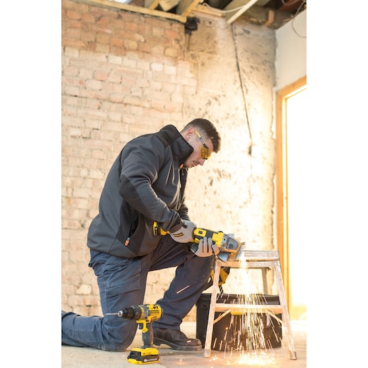 STANLEY FMCK464D2 power tool in use, worker cutting metal with grinder, drill on floor, construction site background.