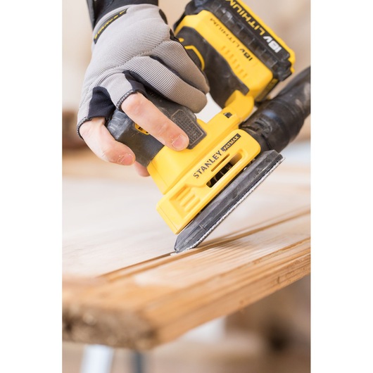 Photo of STANLEY FMCW210B cordless sander being used on wood surface, close-up angle.