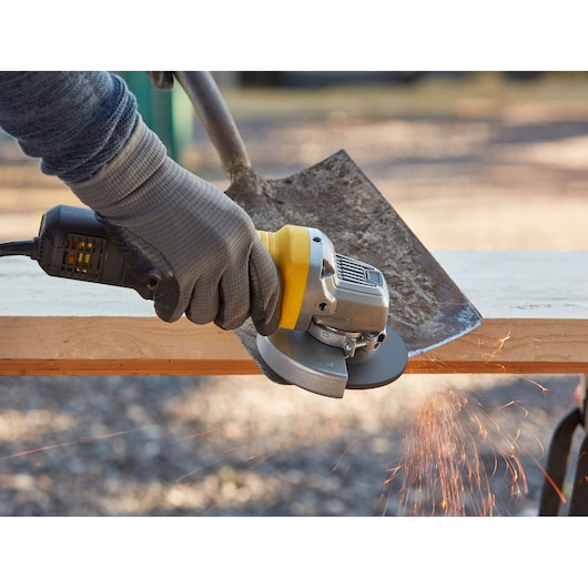 STANLEY FMEG210K angle grinder in use, grinding a shovel edge, emitting sparks, close-up photo.