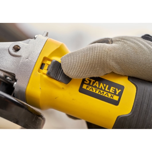 STANLEY FMEG225VS angle grinder close-up with gloved hand pressing power switch, yellow and black body.