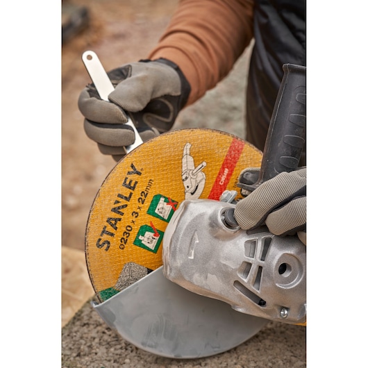 STANLEY FMEG232 angle grinder side view, showing gloved hands adjusting blade outdoors.