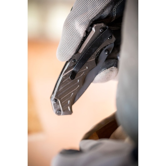 Close-up photo of a gloved hand holding a STANLEY FMHT0-10311 folding utility knife with black handle.
