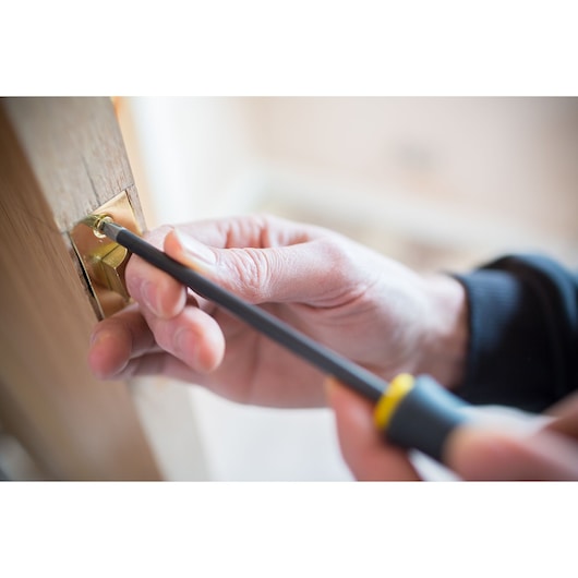 Photo of STANLEY FMHT0-62062 screwdriver in use fixing a brass plate on a wooden door frame.