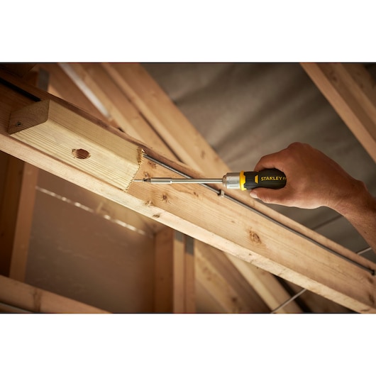 Stanley FMHT0-62690 screwdriver used to fasten screw into wooden beam, closeup in construction setting.