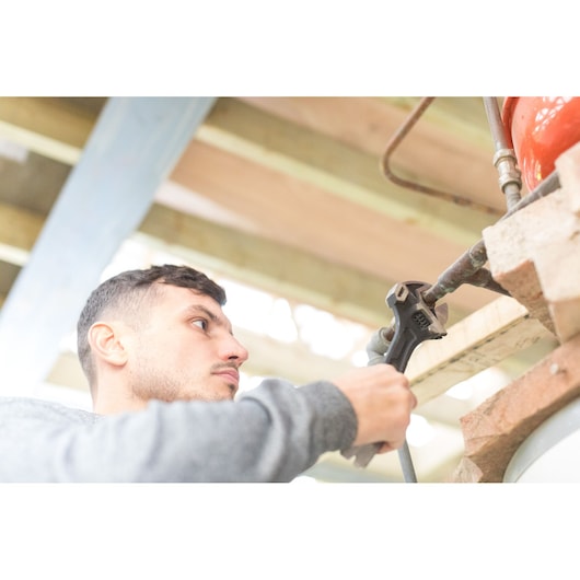 STANLEY FMHT0-75081 adjustable wrench held by a person tightening a pipe in workshop setting.