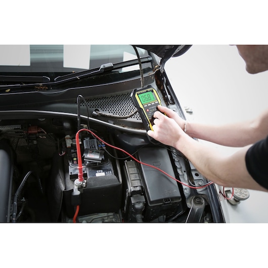 Photo of STANLEY FMHT0-77419 automotive multimeter testing a car battery, top view of engine compartment.