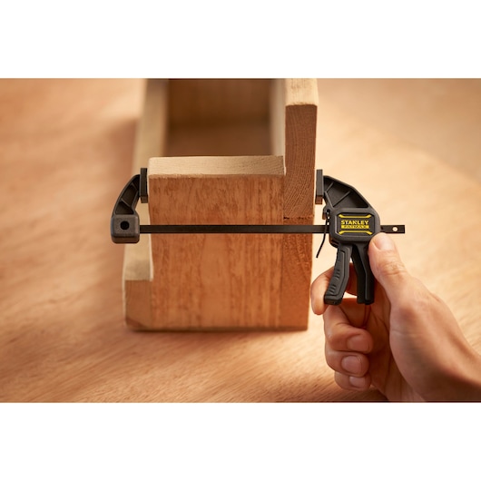 Photo of STANLEY FMHT0-83231 quick clamp holding two wooden pieces, close-up with hand operating clamp.