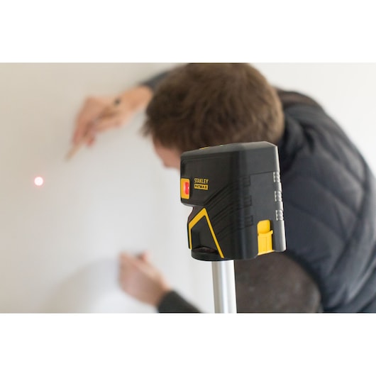 STANLEY FMHT1-77413 laser level tool in use, mounted on tripod, yellow and black design, user marking wall.