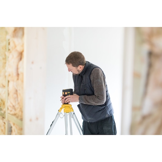 Photo of STANLEY FMHT1-77413 laser level on tripod used by worker in construction setting.
