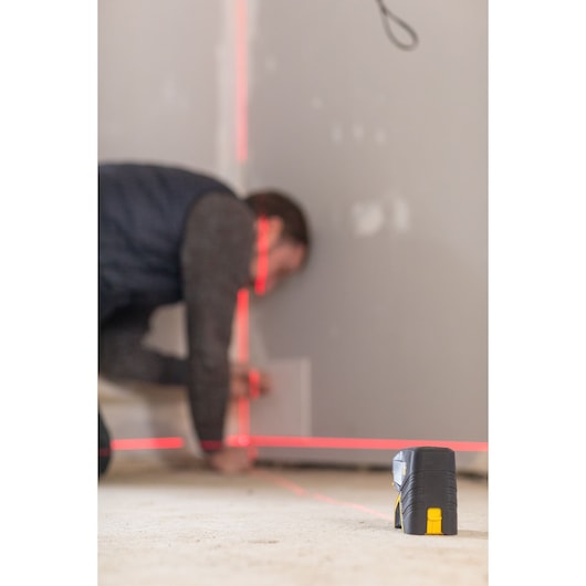 STANLEY FMHT1-77415 laser level projecting red lines on a wall during construction work, product in foreground.