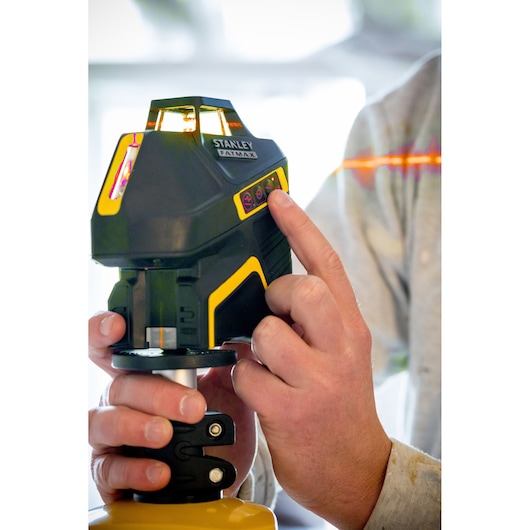 Stanley FMHT1-77416 laser level in use, person adjusting control panel, emitting visible orange laser line.