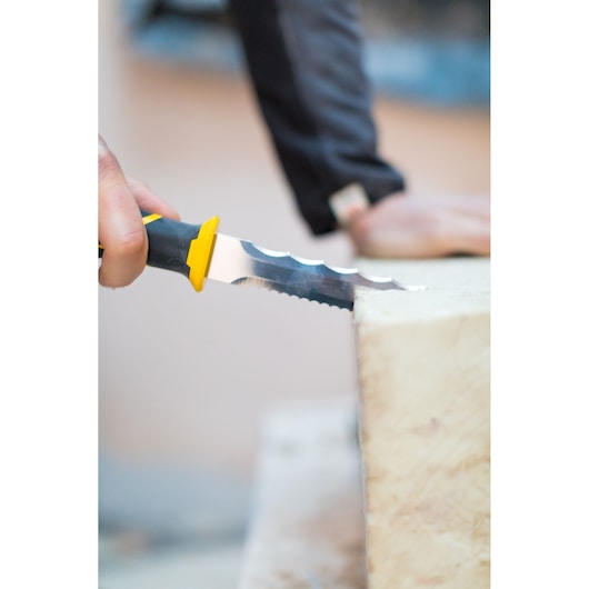 STANLEY FMHT10327-1 insulation knife with yellow and black handle cutting through insulation material, close up.