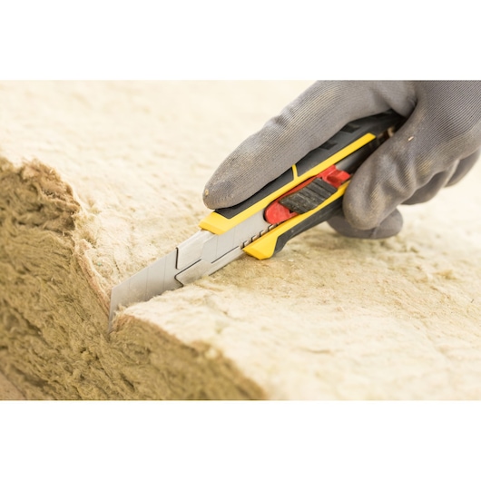 STANLEY FMHT10338-0 utility knife with segmented blade cutting insulation material, close-up view.